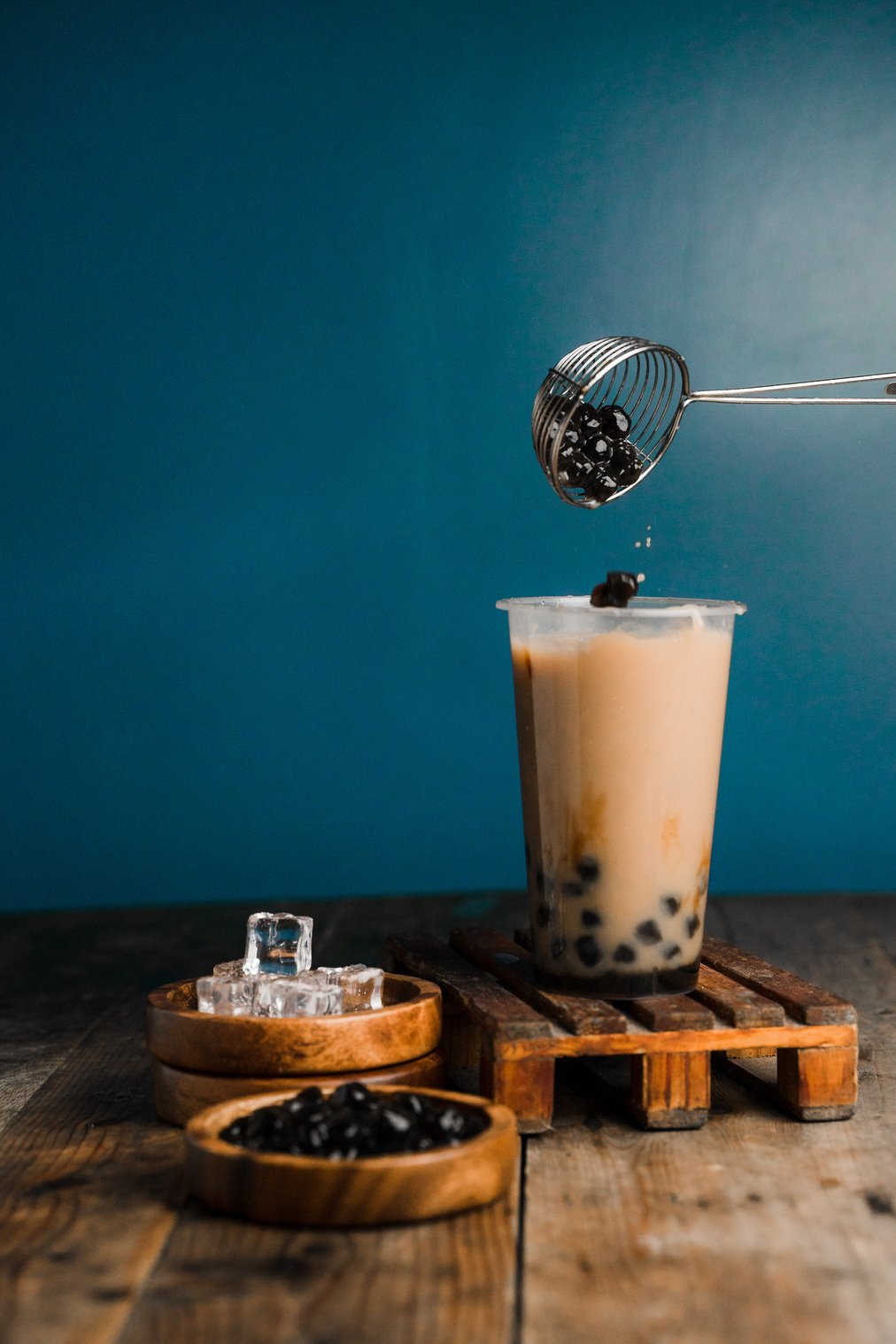 Scoop Pouring Tapioca into Glass of Milk Tea on Table